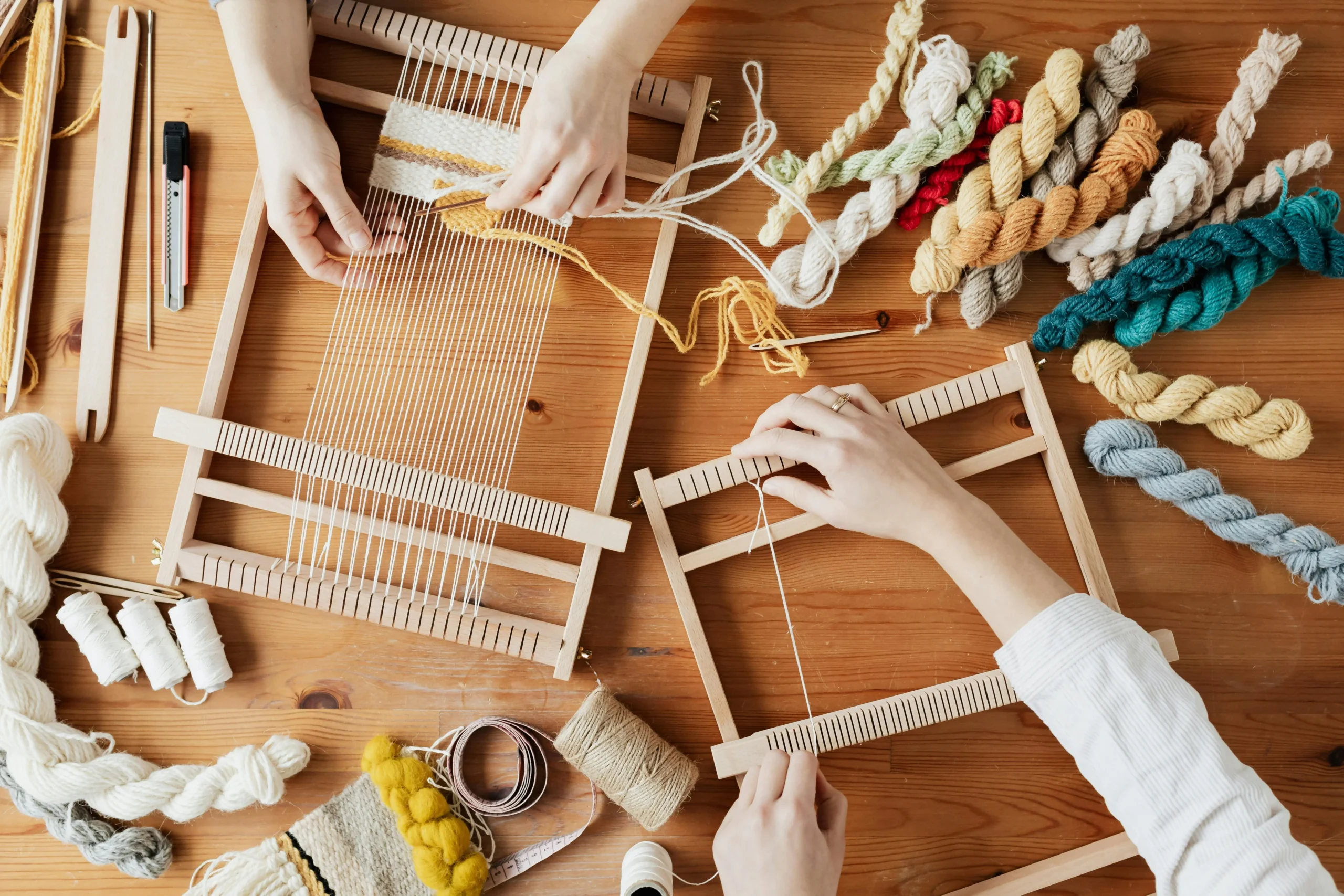 Due persone creano oggetti di artigianato su un tavolo in legno. Sul tavolo sono presenti dei fili colorati.